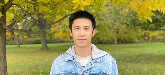 Chen Wang in front of fall-colored trees