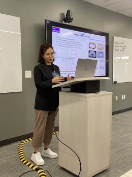 Misun Min stands at a podium with her slides displayed on a TV screen behind her