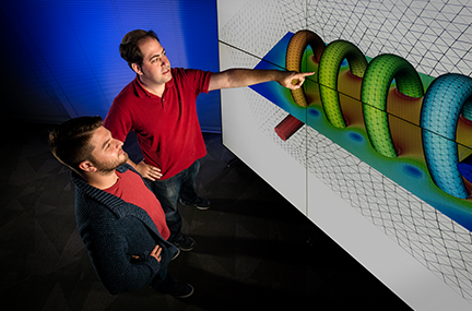 two people, one of them pointing, examine a simulation projected onto a large screen