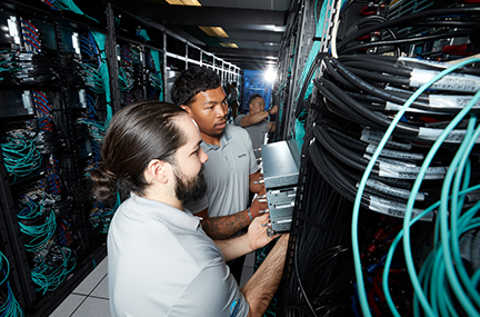 looking down a row of racks with exposed wires, three people install components of El Capitan