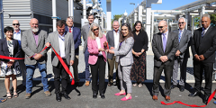 13 people cut a red ribbon in front of the new building