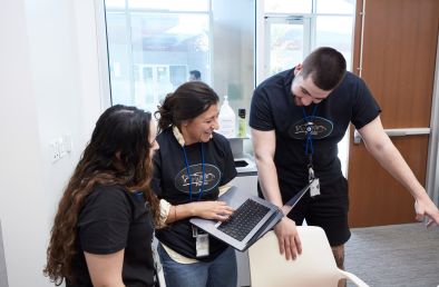 Three smiling people looking at a laptop