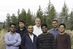 six men pose as a group in front of trees